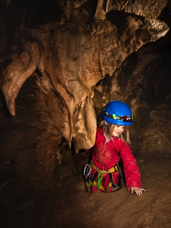 Enfant explorant un passage étroit dans une grotte lors d’une sortie spéléologie dans les Pyrénées-Orientales