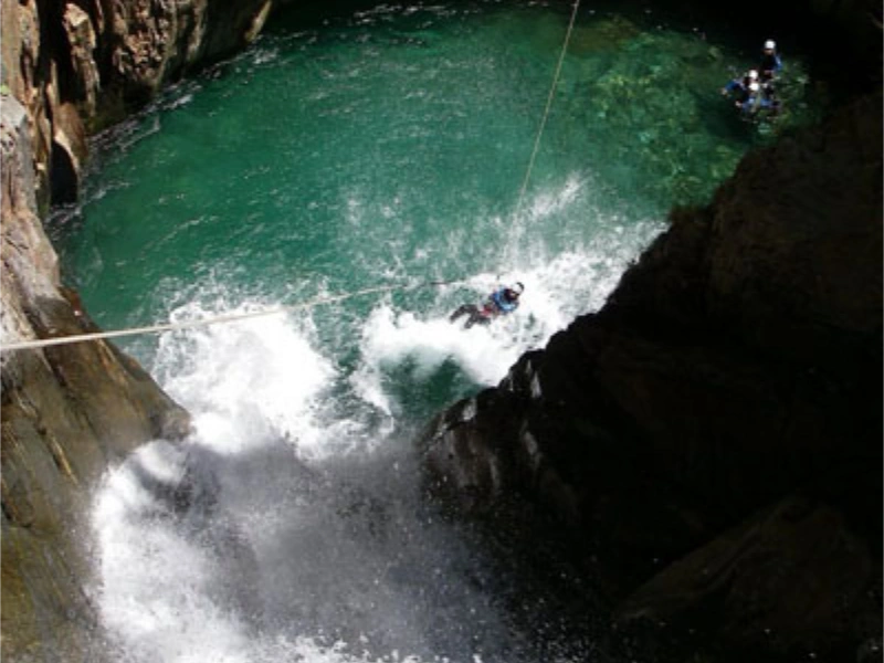 Participant descendant en rappel dans une grande vasque turquoise du canyon de l’Artigue en Ariège dans les Pyrénées
