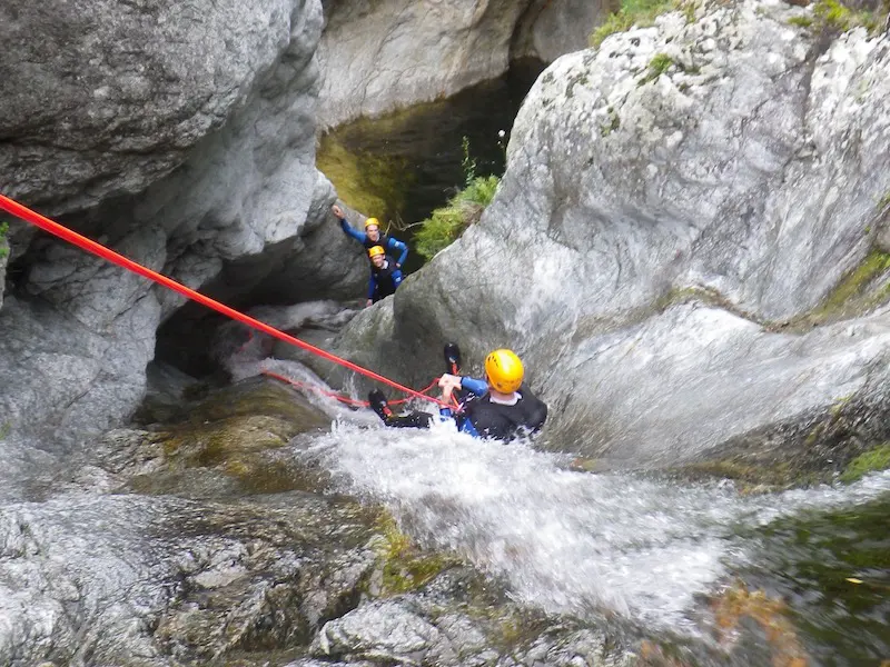 Participant descendant en rappel dans une cascade du canyon du Mas Calsan avec le groupe en attente dans la vasque près de Céret dans les Pyrénées-Orientales.