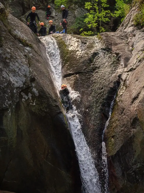 Participant descendant un toboggan naturel dans le canyon du Llech sous le regard du groupe dans les Pyrénées-Orientales